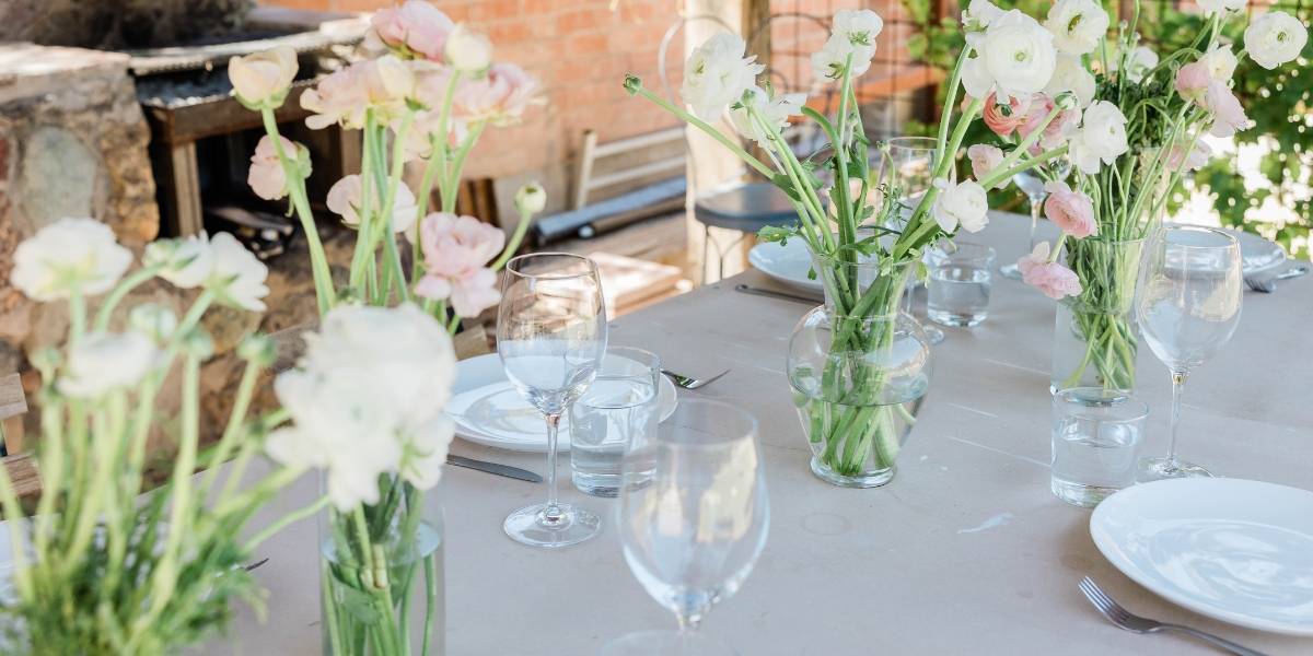 Bild på ett uppdukat bord med blommor. Tips för dukning är att man kan använda sig av vilda blommor som man själv plockat och lägga dem i glas om man inte har tillräckligt många vaser. Bilden visar exempel på detta